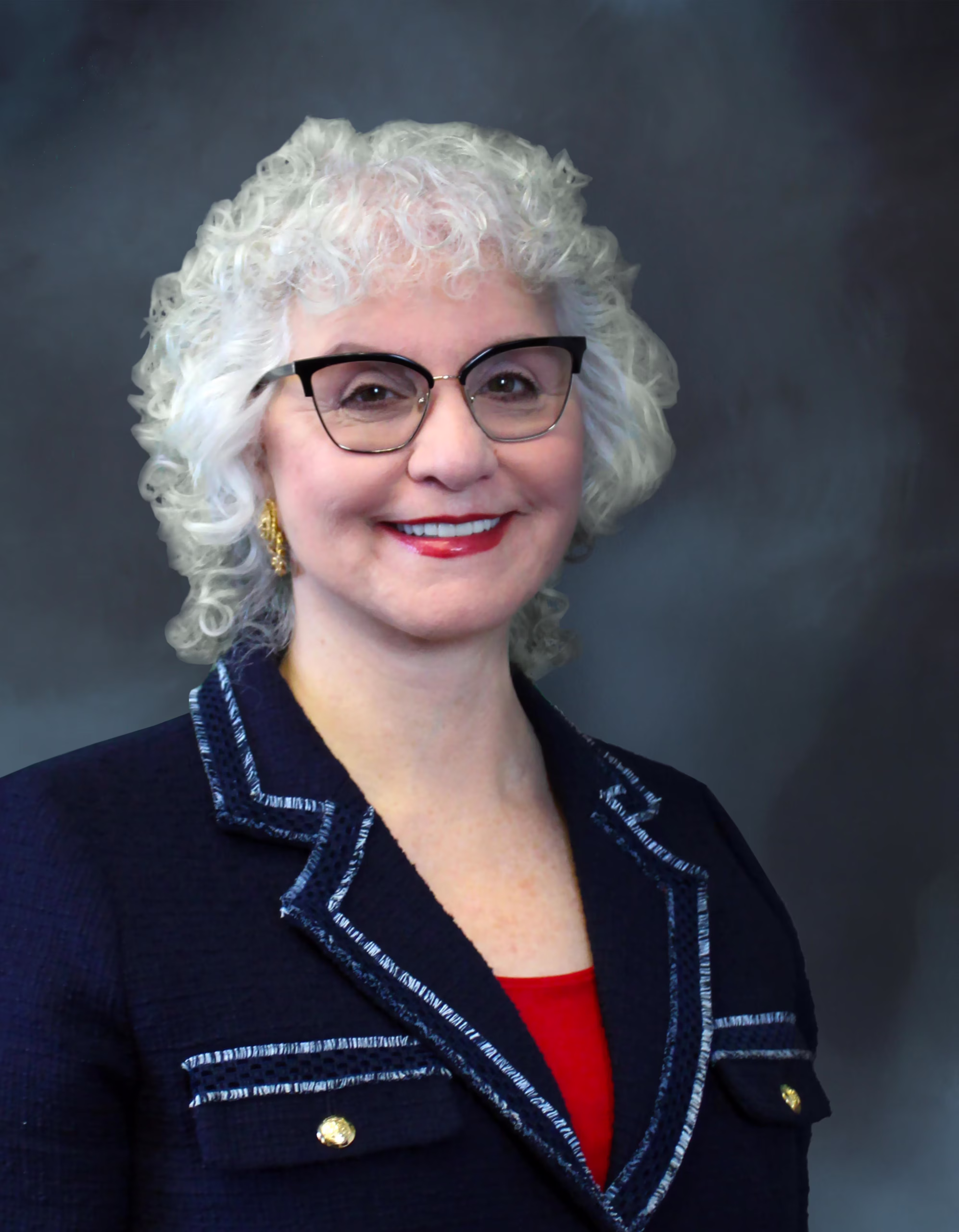 Official 2025 portrait of Senecal, a smiling woman with curly white hair and black-framed glasses wearing a navy tweed blazer with gold buttons over a red top against a gray backdrop